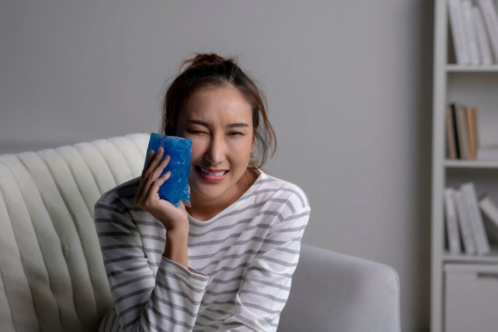Woman in striped shirt squinting in pain holding ice pack to face